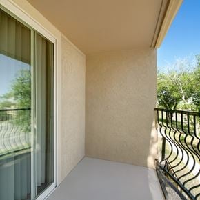 Midland apartment for rent - A private outdoor balcony here at Avalon Springs with a covered ceiling, textured neutral walls, and a sliding glass door, featuring a black metal railing and peaceful views of surrounding greenery for a quiet, relaxing outdoor retreat.