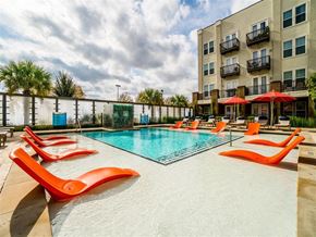 Garland apartment for rent - A pool surrounded by orange chairs and a building in the background.