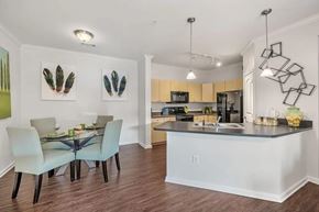 Austin apartment for rent - A bright dining and kitchen area here at Canyon Vistas with a glass-top dining table, upholstered chairs, light wood cabinets, dark countertops, pendant lighting, and an open-concept layout.