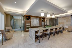 Dallas apartment for rent - A resident lounge here at Cityplace Heights with a long stone island table, cushioned bar chairs, pendant lights, built-in appliances, tan tile flooring, and nearby seating areas with beige lounge chairs and glass-walled meeting room.