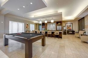 Dallas apartment for rent - A game lounge here at Cityplace Heights with a pool table, long bar-height counter with stools, pendant lights, tile floors, and adjacent seating areas with soft chairs and tables.