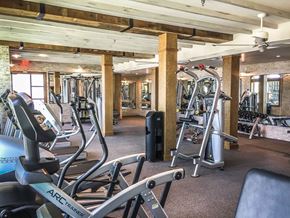 Farmers Branch apartment for rent - A spacious fitness center here at Crosby at the Brickyard with modern cardio and strength equipment, warm wood beam ceilings, mirrored walls, and bright lighting, creating an inviting and energizing workout space.