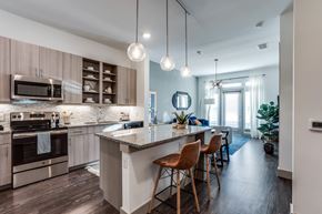 Farmers Branch apartment for rent - A bright kitchen and dining area here at Crosby at the Brickyard with granite island, warm wood cabinets, pendant lights, and cozy bar stools, creating a clean, modern, welcoming space.