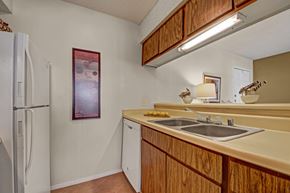 Midland apartment for rent - A compact kitchen here at Cypress Pointe with warm wood cabinets, beige countertops, and a double stainless steel sink beneath bright overhead lighting. White appliances, including a refrigerator and dishwasher, add a clean, functional feel to this cozy, practical cooking space.