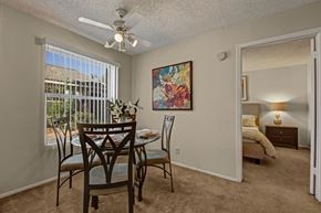 Midland apartment for rent - A bright dining area here at Cypress Pointe with beige carpet, neutral walls, and a large window with vertical blinds bringing in natural light. A ceiling fan adds comfort, while the open layout offers a clear view into the bedroom, creating a warm and inviting space for everyday dining.