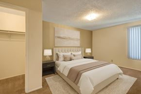 Odessa apartment for rent - A comfortable bedroom here at Fairgreen with plush beige carpet, soft neutral walls, and a large window with vertical blinds bringing in natural light. A neatly staged bed with neutral bedding and an adjacent walk-in closet create a calm, inviting, and functional retreat.