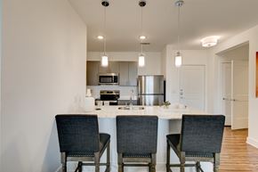 Rockwall apartment for rent - A modern kitchen here at Florence at the Harbor with a quartz island, pendant lighting, bar seating, gray cabinets, and stainless steel appliances, creating a bright, stylish cooking and dining space.