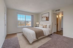 Odessa apartment for rent - A bright, spacious bedroom here at Golden Crest with plush carpeted flooring, a neatly made bed in soft neutral tones, and a large window with vertical blinds that allows natural light to fill the room, creating a calm and comfortable retreat with easy access to the adjoining hallway and bathroom.