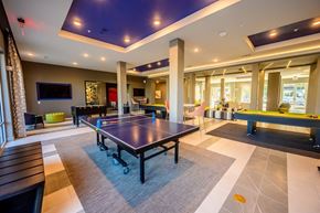 Rowlett apartment for rent - A modern game room here at Harmony Luxury featuring a ping pong table, pool tables, lounge seating, and mounted TVs, enhanced by stylish lighting, open layout, and a lively, social atmosphere for residents to enjoy.