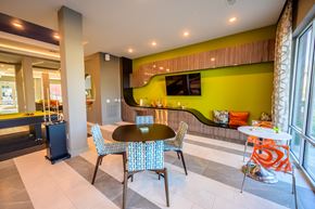 Rowlett apartment for rent - A vibrant community lounge here at Harmony Luxury with modern seating, colorful accent chairs, a built-in refreshment area, and a mounted TV, enhanced by natural light and contemporary design elements that create a fun, social atmosphere.