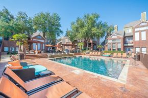 Dallas apartment for rent - A resort-style outdoor pool here at Lakewood on the Trail with clear blue water, spacious sun deck, lounge chairs, shaded seating areas, and surrounding brick buildings, creating a bright, relaxing community space.