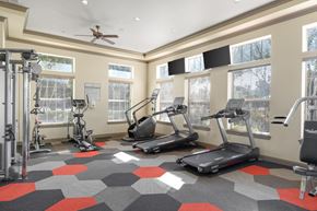 Mansfield apartment for rent - A fitness room here at Landing at Mansfield with treadmills, ellipticals, weight machines, and gray-and-red hex tile flooring, plus large bright windows and wall-mounted TVs.