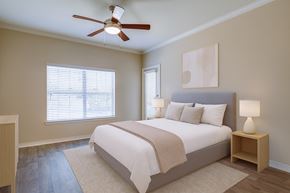 Mansfield apartment for rent - A bedroom here at Landing at Mansfield with a gray upholstered bed, white bedding with beige throw, light wood nightstands, matching white lamps, neutral wall art, and warm wood flooring with a soft cream rug.