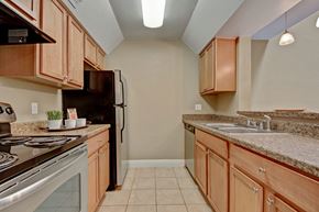 Midland apartment for rent - A compact kitchen here at Las Colinas with light wood cabinets, speckled countertops, and a stainless steel sink. Black appliances, tile flooring, and overhead lighting create a clean, functional space with a warm, neutral tone.