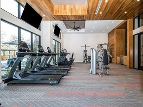 Allen apartment for rent - A modern fitness center here at Magnolia on the Green with treadmills, strength machines, high ceilings with wood accents, wall-mounted TVs, and large windows bringing in natural light for an open, energizing workout space.