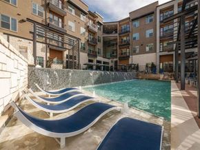 Allen apartment for rent - A resort-style pool area here at Magnolia on the Green with in-water lounge chairs, a cascading water feature wall, surrounding apartment buildings with balconies, and sunny deck space for relaxing outdoor enjoyment.