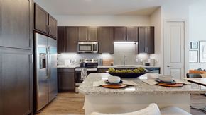 Allen apartment for rent - A modern kitchen here at Magnolia on the Green with dark wood cabinets, granite countertops, stainless steel appliances, a center island with seating, and bright under-cabinet lighting for a clean, upscale feel.