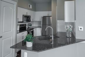 Fort Worth apartment for rent - A modern kitchen here at Monterra Village with white cabinets, dark granite countertops, stainless steel appliances, a subway tile backsplash, and a peninsula sink with bar-style counter space for a clean, bright look.