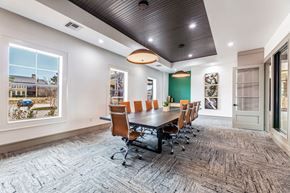 Fort Worth apartment for rent - A conference room here at Monterra Village with a long dark table, brown leather swivel chairs, green accent wall, black ceiling detail, and large bright windows along the side.