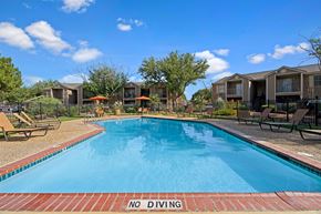 Midland apartment for rent - A sunny outdoor swimming pool here at Northridge Court surrounded by a spacious pool deck with lounge chairs, patio umbrellas, and landscaped greenery, with nearby apartment buildings, mature trees, and a clear blue sky creating a relaxing community setting.