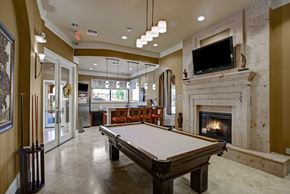 Midland apartment for rent - A stylish resident lounge here at Palms at Briarwood featuring a pool table, stone fireplace, mounted television, and bar seating, with pendant lighting, polished floors, and an open layout creating a welcoming space for relaxing, socializing, and entertaining guests.