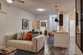 Austin apartment for rent - A living and kitchen space here at Reserve at Arboretum with a beige sofa and colorful accent pillows, dark wood floors, and a bright island with pendant lights, creating a warm, modern, and inviting open layout.