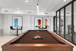 Austin apartment for rent - A game lounge here at Reserve at Arboretum with a dark wood pool table and brown felt, bright modern lighting, colorful boot artwork, and small café tables, creating a clean, social, and welcoming hangout space.
