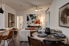 Austin apartment for rent - A dining and living area here at Reserve at Arboretum with a round dark wood table, brown leather chairs, a beige sofa with colorful accent pillows, and warm modern artwork, creating a bright, stylish, and welcoming open space.