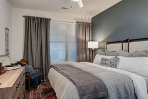 Austin apartment for rent - A bedroom here at Reserve at Arboretum with a dark green accent wall, upholstered headboard, layered gray and white bedding, warm wood dresser, and patterned rug, creating a cozy, modern, and inviting retreat.