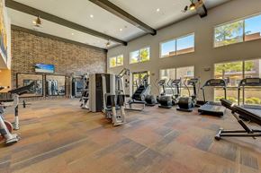 Dallas apartment for rent - A fitness center here at Skyline Farmers Market with large windows, brick accent wall, treadmills and ellipticals, strength machines, mirrors, and high ceilings with exposed beams and bright natural light.
