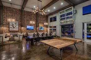 Dallas apartment for rent - A resident lounge here at Skyline Farmers Market with brick accent walls, dark wood beams, long community table, wood table tennis table, warm chandelier lighting, and modern seating areas opening to an outdoor pool patio.