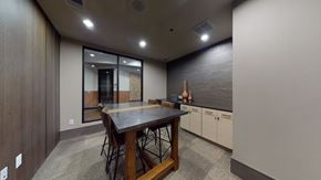 Fairview apartment for rent - A work lounge here at Sorrel Fairview with a tall dark wood table, brown leather stools, stone-look tabletop, light wood cabinets, and a sleek accent wall, creating a modern, quiet meeting space.