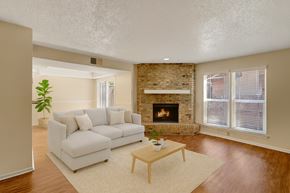 Odessa apartment for rent - A bright, inviting living room here at Summertree Place featuring warm wood-style flooring, a neutral sectional sofa with soft pillows, a light area rug, and a simple coffee table, complemented by a brick fireplace, large windows with blinds, and an open layout that allows natural light to fill the space.
