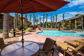 Odessa apartment for rent - A resort-style outdoor pool area here at Tuscany at Faudree featuring a sparkling curved swimming pool surrounded by palm trees, tan lounge chairs, and shaded seating under large umbrellas. Warm-toned buildings, landscaped greenery, and a sunny blue sky create a relaxing, vacation-inspired community atmosphere.