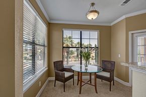 Odessa apartment for rent - A bright dining nook here at Tuscany at Faudree with plush carpet and neutral walls. A small round glass-top table with two chairs sits beneath a ceiling light, while large windows with blinds bring in natural light and views of surrounding greenery, creating a cozy space for everyday meals.