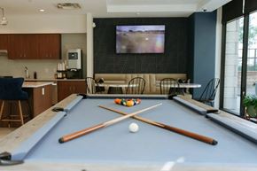 Lewisville apartment for rent - A stylish resident lounge here at Valor at the Realm with a pool table, modern seating booths, café-style tables, a coffee station, and a wall-mounted TV, featuring large windows and a social, upscale atmosphere.