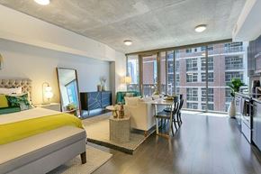Dallas apartment for rent - A bright studio-style apartment here at Victory Place with floor-to-ceiling windows, dark wood flooring, a modern kitchen, cozy living area, and a sleeping space with green accent bedding and stylish decor.