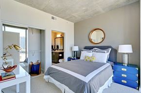 Dallas apartment for rent - A bedroom here at Victory Place, including a nighstand, modern lamp, a mirror above the bed, with a sliding  closet in the wall. The space is encompassed by bright natural light