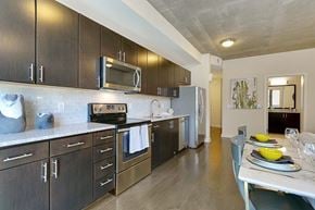Dallas apartment for rent - A sleek galley-style kitchen here at Victory Place with dark wood cabinets, stainless steel appliances, a tile backsplash, modern countertops, and a nearby dining table set for four.