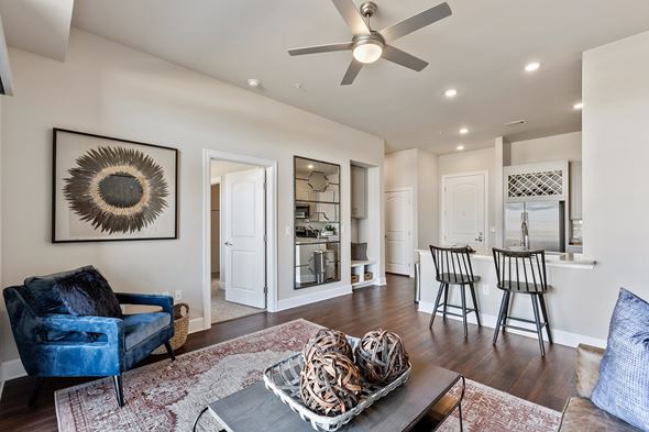 Frisco apartment for rent - A modern open living area here at Waterford Market with dark wood flooring, a ceiling fan, accent chair, decorative wall art, and a breakfast bar with seating that connects to the bright kitchen.
