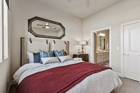 Frisco apartment for rent - A cozy bedroom here at Waterford Market with soft carpet, a padded headboard bed, layered accent pillows, a bedside lamp, and a private bathroom entrance just off the room.