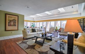 Midland apartment for rent - A bright community lounge here at Wildflower showcasing a spacious seating area with comfortable sofas and patterned armchairs arranged around a coffee table, warm wood-style flooring, decorative rugs, and large windows that bring in abundant natural light, creating an inviting space for residents to relax or gather.