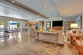 Salt Lake City apartment for rent - A game and lounge room here at Bridges with tan sofas, wood accent tables, ping pong table, bar-height kitchen counter with stools, TV wall, and polished concrete floors in a bright, open layout.