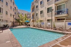 Salt Lake City apartment for rent - A pool courtyard here at Bridges with a rectangular pool, beige apartment buildings, blue balcony railings, tan deck, and lounge chairs, creating a bright, inviting outdoor amenity space.