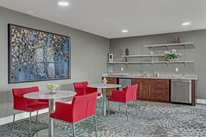 Sandy apartment for rent - A resident café lounge here at Hills at Sandy Station with red accent chairs, round café tables, patterned carpet, large blue wall art, and a refreshment counter with wood cabinets and open shelving.