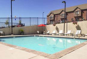 Sandy apartment for rent - A pool with chairs and umbrellas in front of a building.