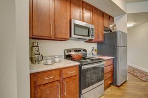 Sandy apartment for rent - A kitchen here at Hills at Sandy Station with rich wood cabinets, stainless steel stove and microwave, gray-speckled countertops, and warm wood-look flooring in a clean, modern layout.