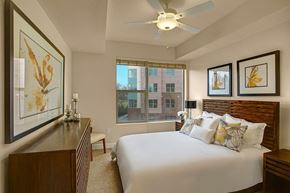 Sandy apartment for rent - A bedroom here at Hills at Sandy Station with a wood bed frame, white bedding with yellow accent pillows, matching wood dresser and nightstands, butterfly wall art, and a bright window view.
