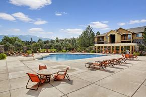 Sandy apartment for rent - A pool area here at Legends at River Oaks with a large blue pool, orange lounge chairs and tables, wide concrete deck, pergola seating, and mountain views under a bright sky.
