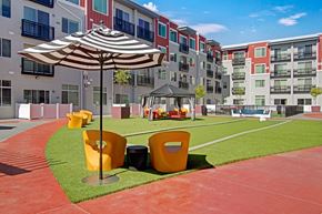 Salt Lake City apartment for rent - A vibrant courtyard lawn here at Ritz Classic with green turf, yellow lounge chairs, striped umbrellas, shaded cabana seating, and modern apartment buildings surrounding the space, creating a bright, social outdoor gathering area.
